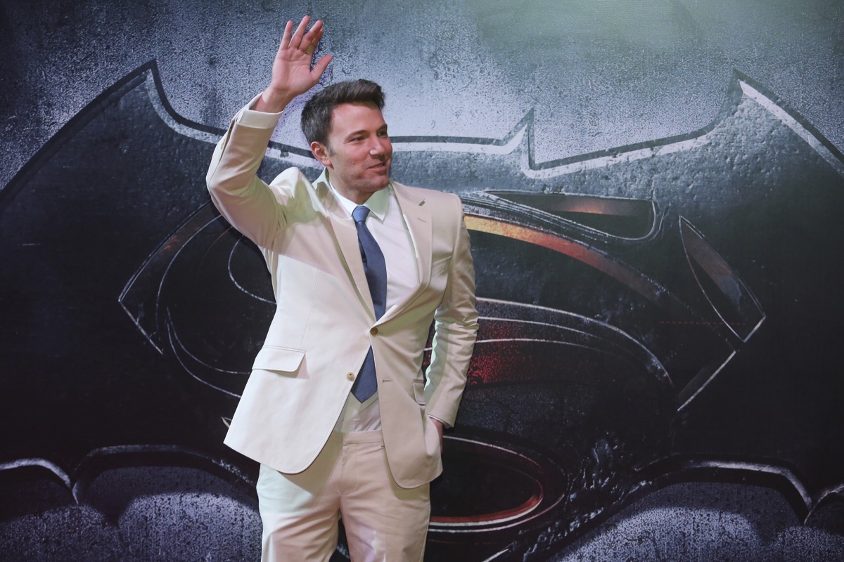 ben affleck waving in a tan suit on a red carpet