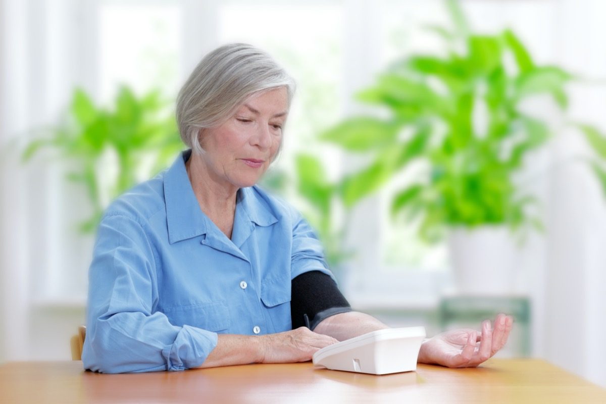 Senior woman suffering from high blood pressure sitting at a table in her living room using a blood pressure monitor