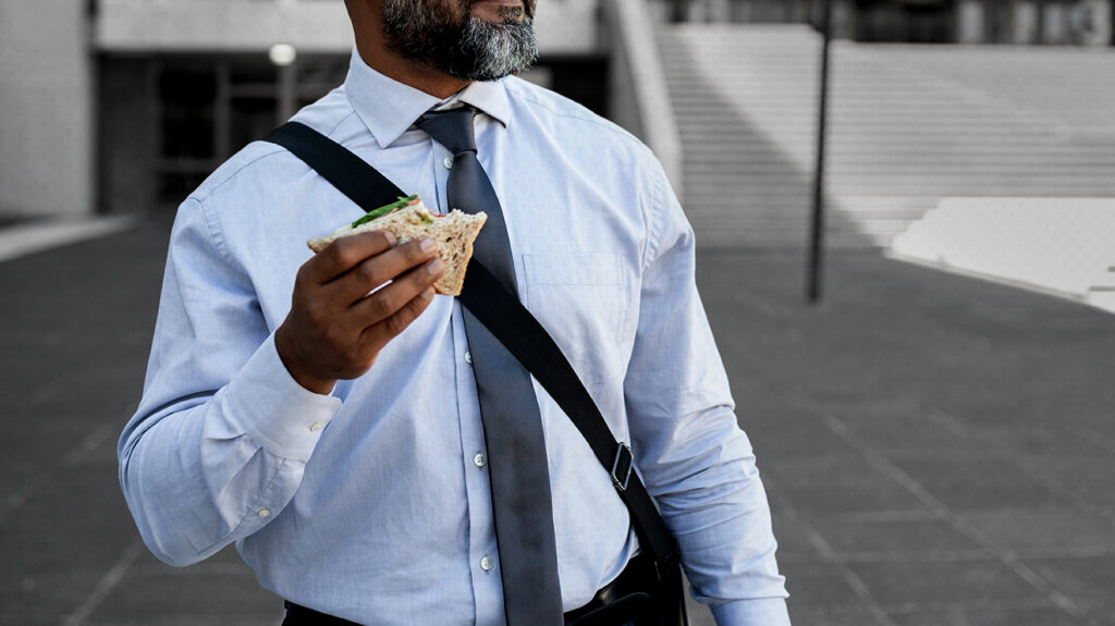 man holding and eating sandwich on his way to work
