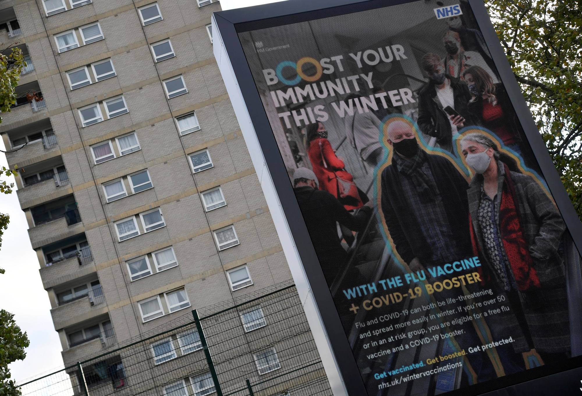 A National Health Service vaccination advertisement near a housing block in London | REUTERS 